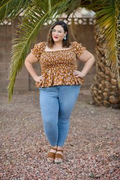 a woman standing in front of a palm tree wearing jeans and a top with an off the shoulder design