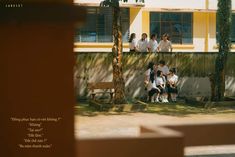 a group of people sitting on top of a bench next to a tree in front of a building