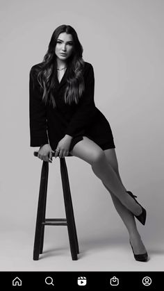 a woman sitting on top of a stool in black dress and high heeled shoes