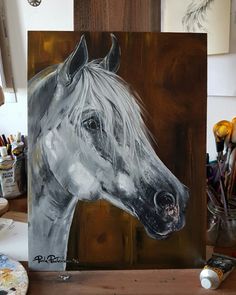 a painting of a white horse on a wooden table next to some paintbrushes