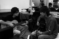 two young men are sitting on the couch playing guitars