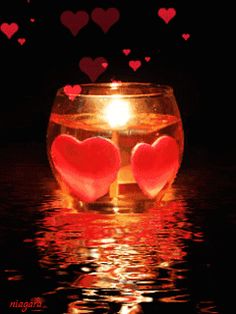 two hearts floating in a bowl of water with the light shining on them and some red candles