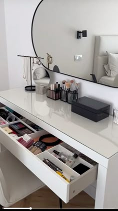 a white desk with drawers underneath a mirror and lights on the wall above it, along with other items