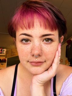 a woman with freckles and piercings on her nose looking at the camera