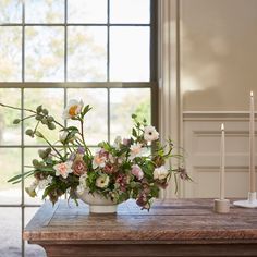 a vase filled with flowers sitting on top of a wooden table next to a window