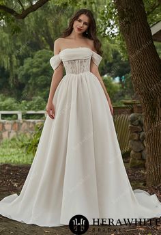 a woman standing in front of a tree wearing a white dress with off the shoulder