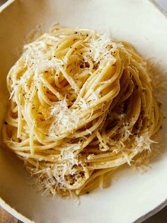 a white bowl filled with pasta covered in parmesan and seasoning on top of a wooden table