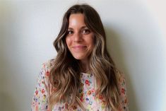 a woman with long brown hair and flowers on her shirt is smiling at the camera