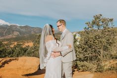 a bride and groom standing together in front of mountains