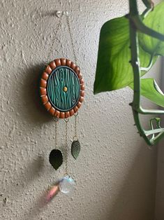 a green and brown clock hanging from the side of a wall next to a plant