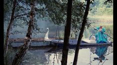 a woman in a blue dress is on a boat with a swan and trees around her