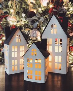 three lit up houses sitting on top of a table next to a christmas tree with lights