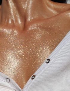 the back of a woman's neck with gold glitter on it and her shirt open