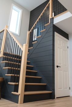 a staircase with black painted walls and wooden handrails in an empty room next to a white door