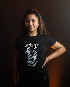 a woman standing in front of a dark background wearing a black shirt with white arrows on it