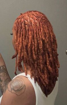 a woman with red dreadlocks is looking at her cell phone in the mirror