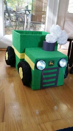 a green tractor made out of foam sitting on top of a wooden floor next to a window