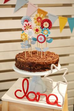 a cake on a table with some flowers and ribbons around it that says love is spelled in red, white, and blue