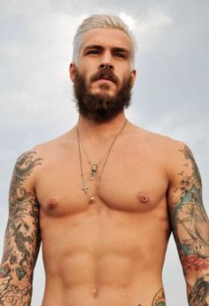 a shirtless man with tattoos on his arms and chest standing in front of the ocean