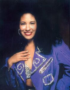 a woman in a purple outfit smiling and posing for the camera with her hands on her chest