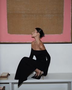 a woman sitting on top of a white bench next to a pink and brown painting