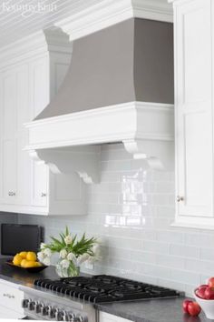 a kitchen with white cabinets and black counter tops, an oven hood over the stove