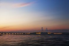 a bridge that is over some water at night with lights in the sky above it