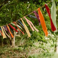 there are many ribbons hanging from the clothes line outside in the woods, and one is orange