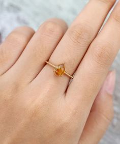 a woman's hand with a yellow ring on top of her finger and an orange stone in the middle