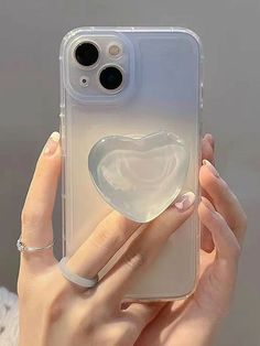 a woman is holding up her phone case with a heart shaped object in the back