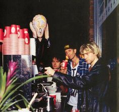 three men are standing at a table with cups on it and one man is pouring something into a cup