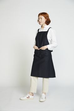 a woman standing in front of a white wall wearing an apron and shoes with her hands on her hips