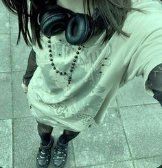 a woman with headphones on her neck is looking down at the ground while wearing a white shirt and black leggings