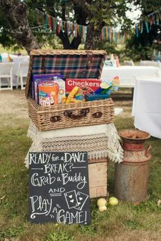 a picnic basket with snacks on it sitting in the grass next to a chalkboard sign