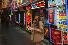 a woman standing on the side of a street next to neon signs