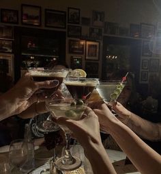 several people holding up wine glasses filled with different types of drinks and garnishes