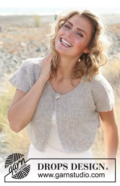 a woman smiling while wearing a cardigan sweater and white dress in front of the ocean