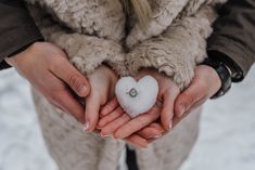 two hands holding a heart shaped item in the middle of it's palms, with snow on them