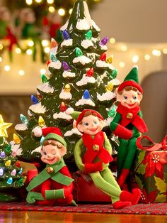 three elf figurines sitting next to a christmas tree