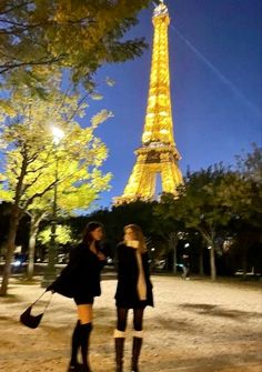 two young women standing in front of the eiffel tower at night, paris