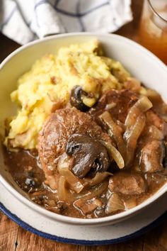 a bowl filled with meat, mushrooms and mashed potatoes on top of a wooden table