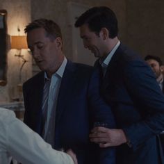 two men in suits are shaking hands with another man who is wearing a white shirt and tie