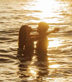 two people are in the water with their arms around each other as the sun sets