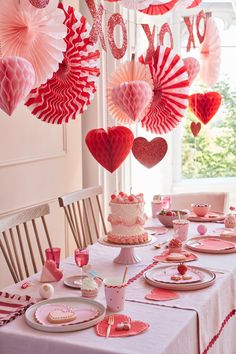 valentine's day table setting with pink and red paper hearts hanging from the ceiling