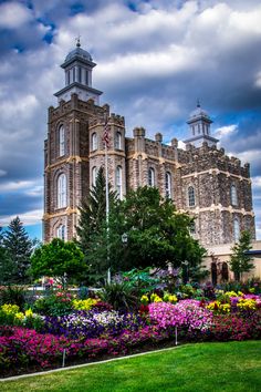 a large building with flowers in front of it and trees around the perimeter, on a cloudy day