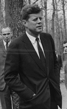 black and white photograph of man in suit walking with other men standing around behind him