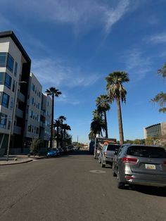 several cars parked on the side of an empty street with palm trees in the background