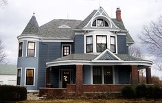 a large blue house with two story windows and an arched roof, on a cloudy day