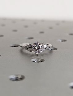 three stone diamond ring sitting on top of a metal surface with drops of water around it