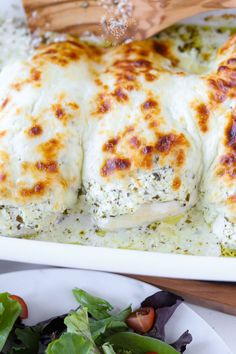 a white plate topped with meat covered in cheese and sauce next to a green salad